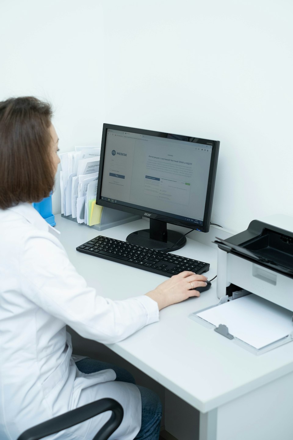 Medical professional works at a computer in a busy office.